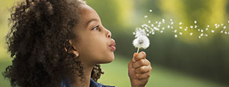 A young person blowing on a flower